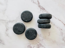 Load image into Gallery viewer, Round, solid shampoo bar that weighs 50g each, made with tea tree essential oil and naturally coloured black with activated charcoal
